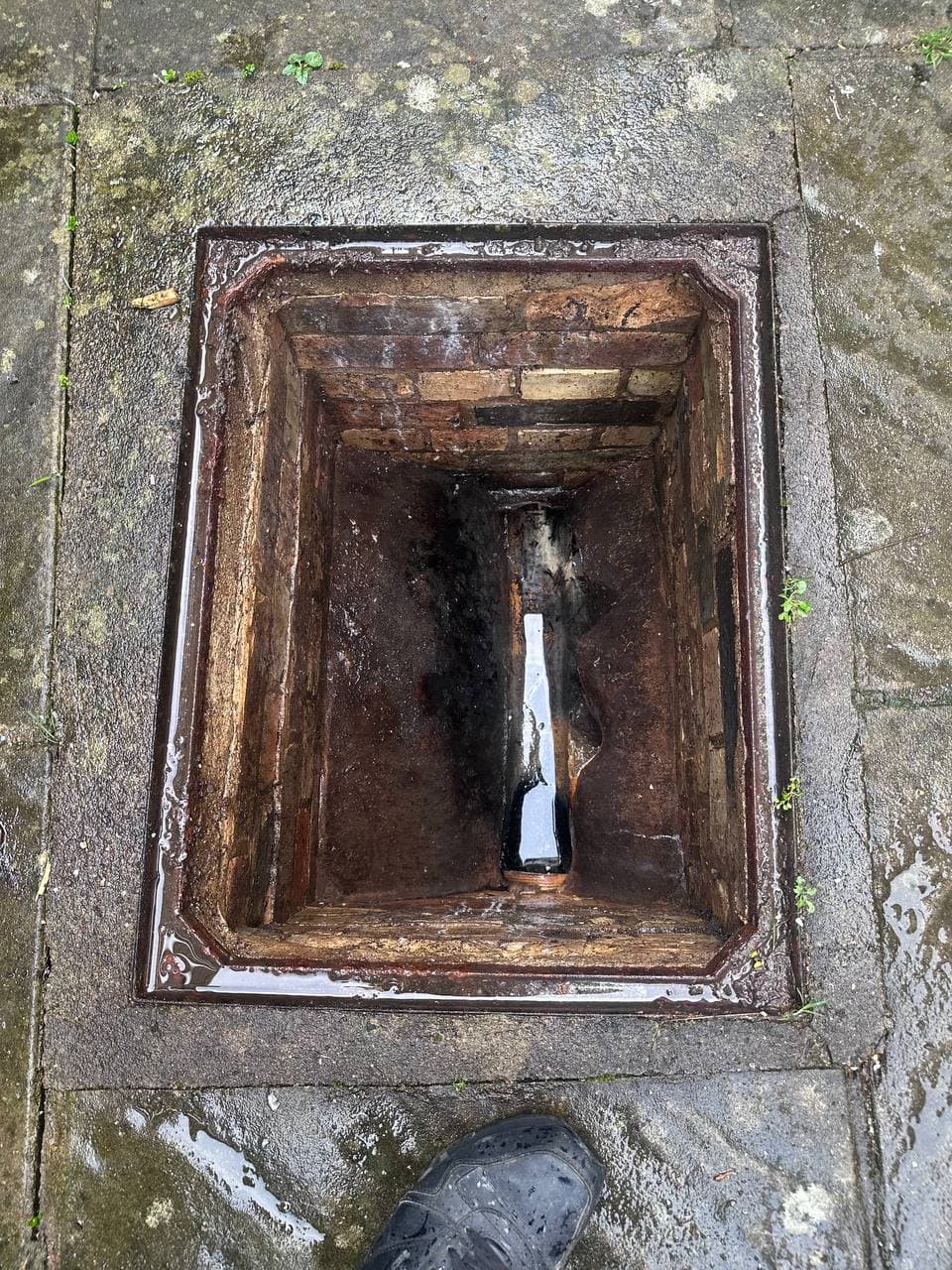 A brick drain inspection chamber with its cover lifted, showing the channel at the bottom