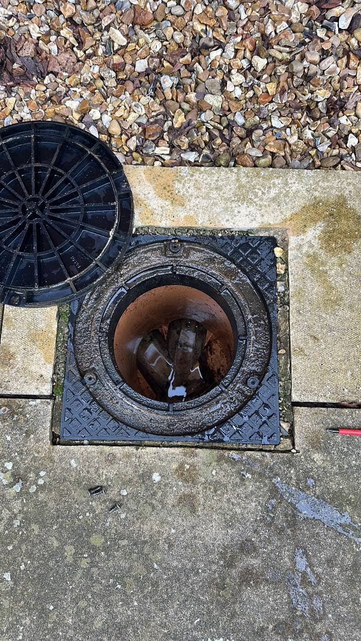 A round plastic drain access chamber outside a property, with its lid lifted off