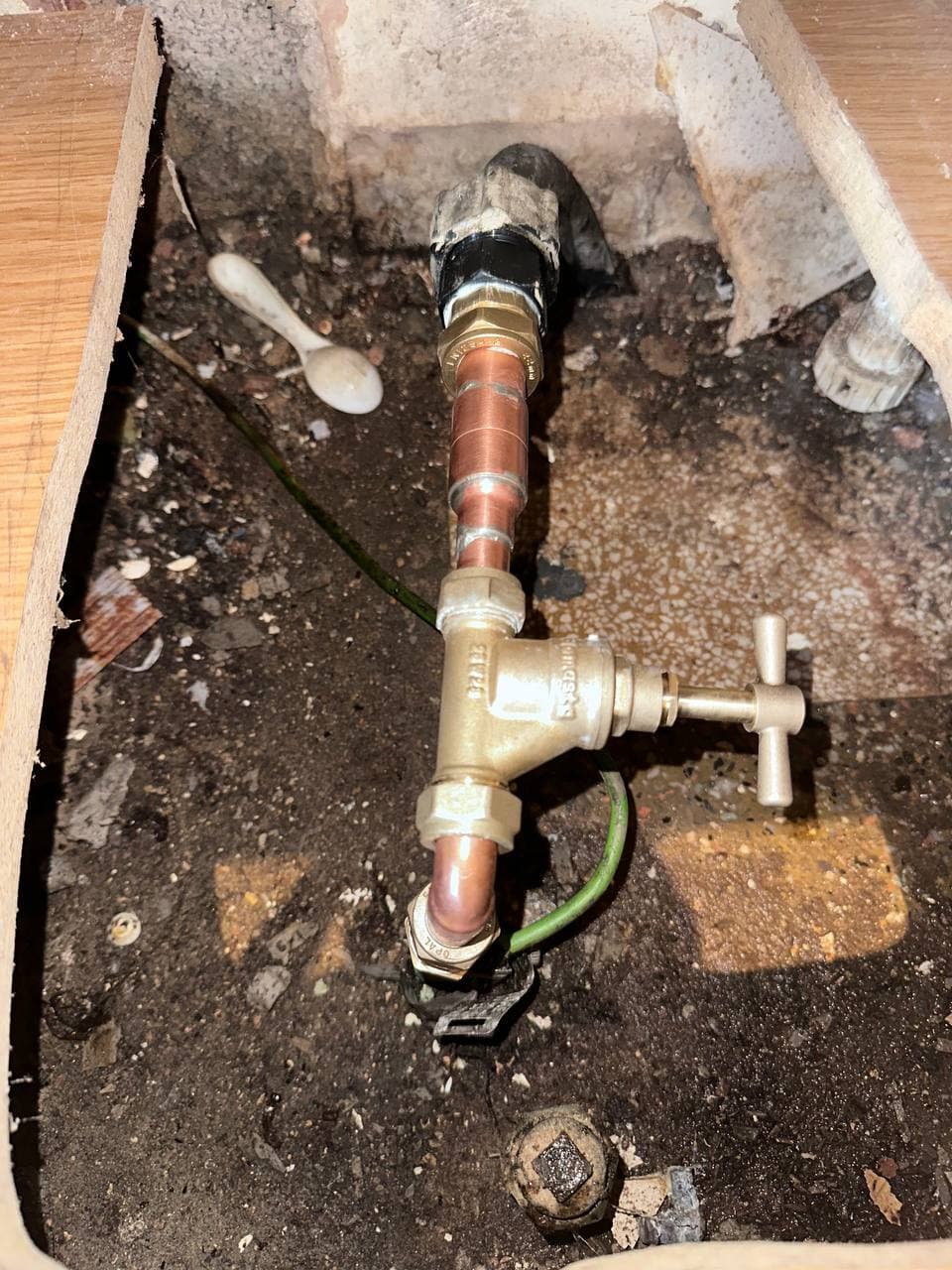 A brass stopcock and copper pipe in the void beneath a floor