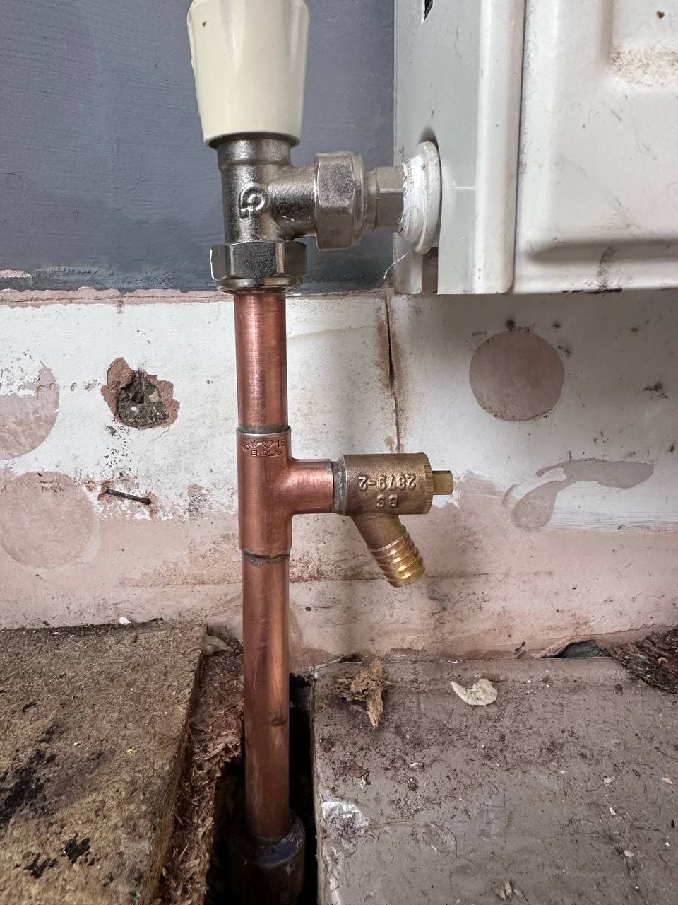 New copper pipe and a drain-off valve feeding a radiator, with the floor opened up