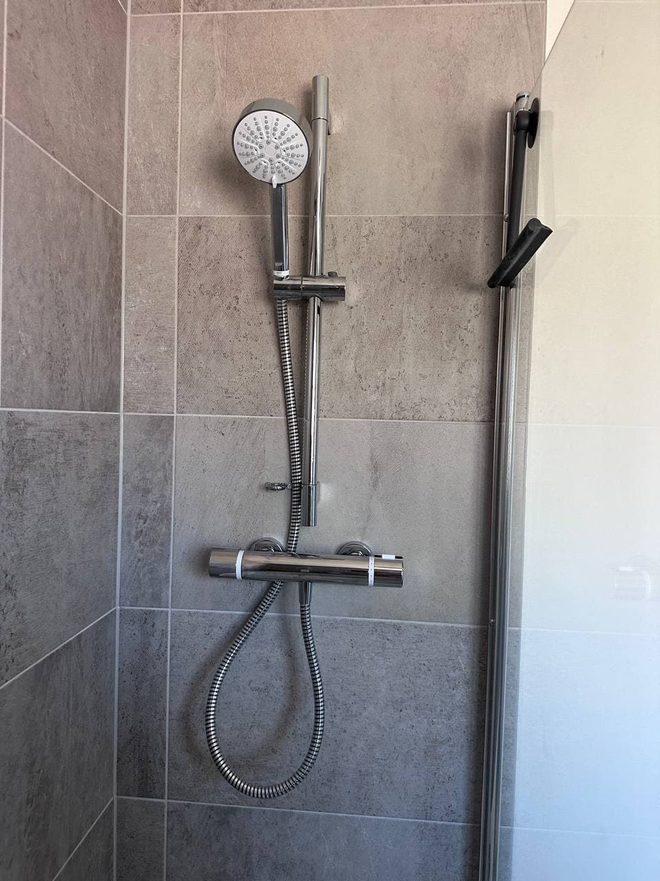 A thermostatic bar shower with a slide rail and handset on grey tiles