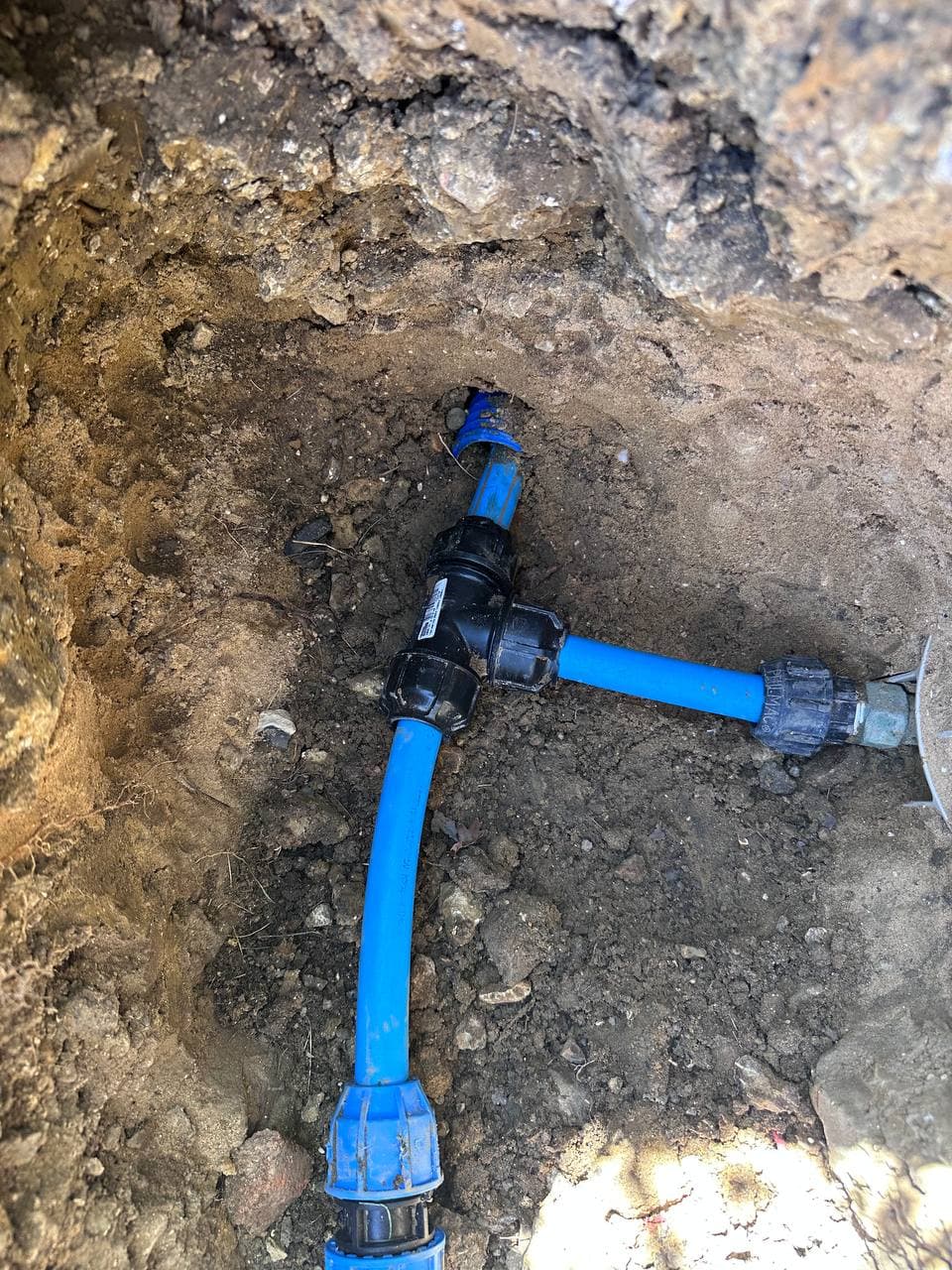 Blue water supply pipe and a joint, exposed in a dug-out section of ground